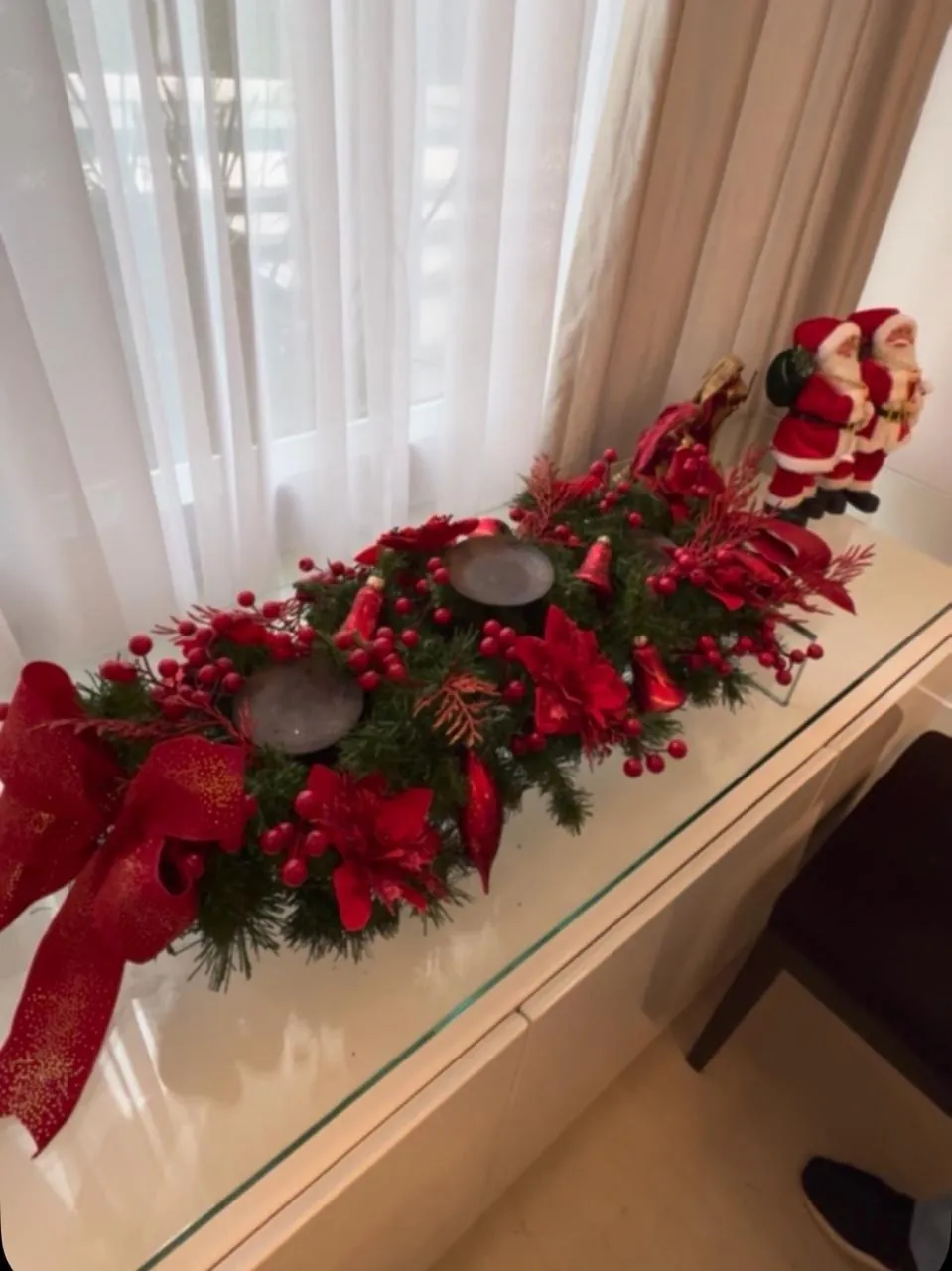 Arranjo natalino com ramos, flores vermelhas e velas sobre aparador de vidro