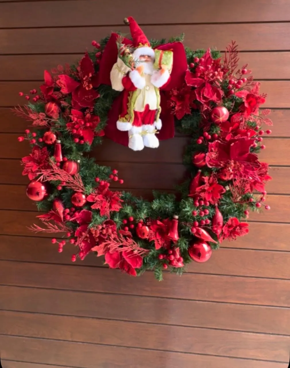 Guirlanda com flores vermelhas e Papai Noel ao centro sobre parede de madeira
