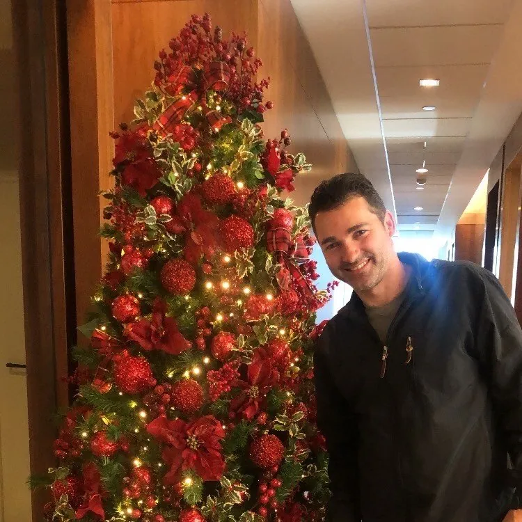 Regis Motta ao lado de uma árvore de Natal decorada